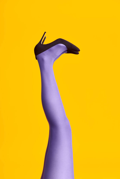 Raised females legs in bright tights and stylish high heels shoes on yellow background - Foto, Imagen