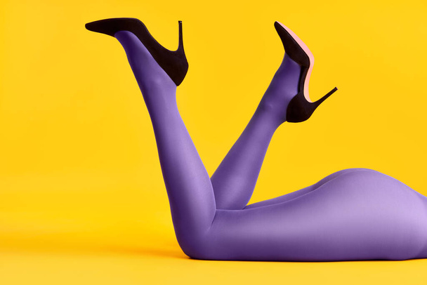 Legs of beautiful young woman wearing bright tights and high heels shoes lying on bright yellow background. - Fotografie, Obrázek