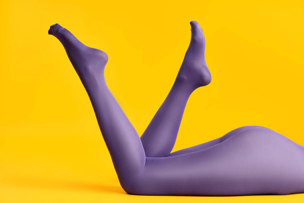 Slim legs of beautiful young woman in bright purple tights relax on yellow background - Foto, imagen