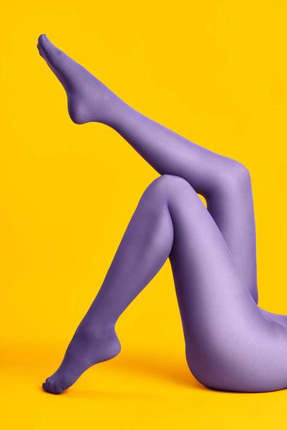 Long legs of beautiful young woman in bright tights relax on yellow background - Фото, изображение