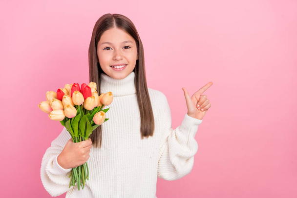 Photo of cute pretty preteen girl dressed white pullover holding flowers bouquet pointing empty space isolated pink color background - Foto, imagen