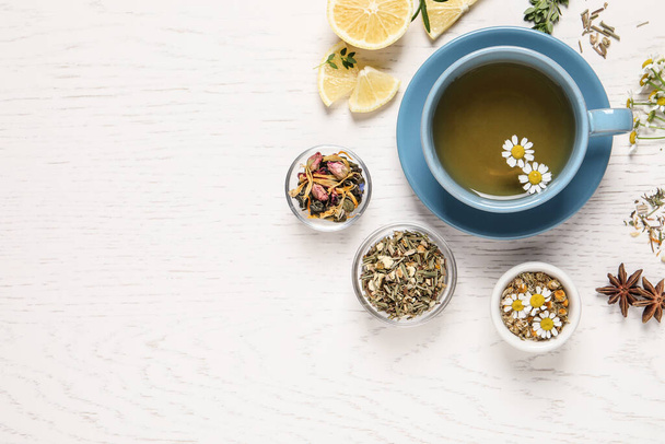 Flat lay composition of freshly brewed tea with chamomile flowers and dry leaves on white wooden table. Space for text - Foto, imagen