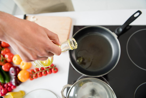 Καλλιεργημένη φωτογραφία άνθρωπος μαγείρεμα προσθέτοντας λάδι στο τηγάνι - Φωτογραφία, εικόνα