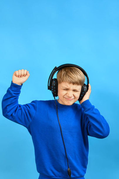 Ein fröhlicher und emotionaler Junge hört Musik über Kopfhörer und tanzt mit den Armen herum. - Foto, Bild
