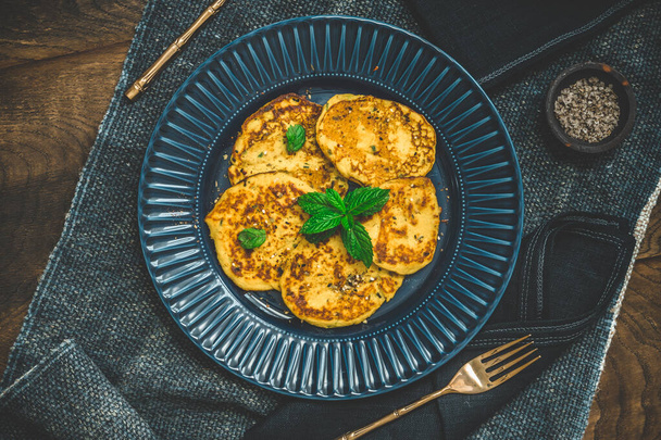 Small pancakes with herbs on a blue plate on rustic wooden background, top view - Valokuva, kuva