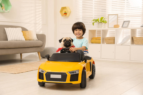 Little boy with his dog in toy car at home - Φωτογραφία, εικόνα