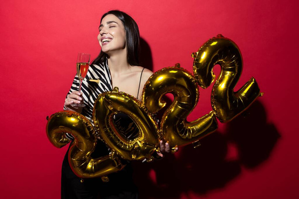 Молодая веселая женщина держит номера 2022 и бокал шампанского - Фото, изображение