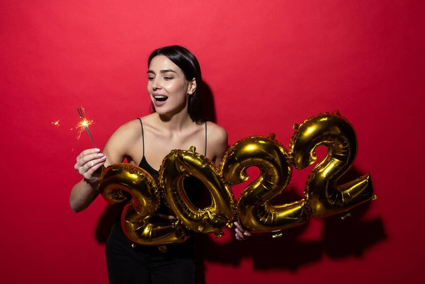 A young cheerful woman in a black dress holds the numbers 2022 and sparklers. - Photo, Image