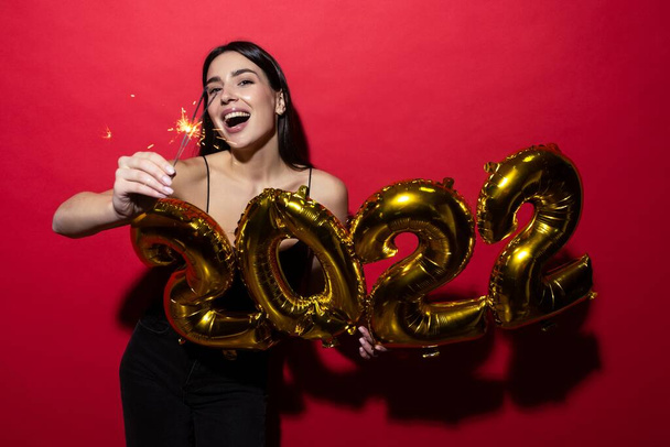 Una joven mujer alegre en un vestido negro sostiene los números 2022 y chispas. - Foto, imagen