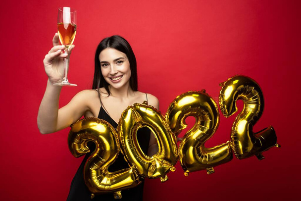 Une jeune belle femme en robe noire tient les numéros 2022 et une coupe de champagne - Photo, image