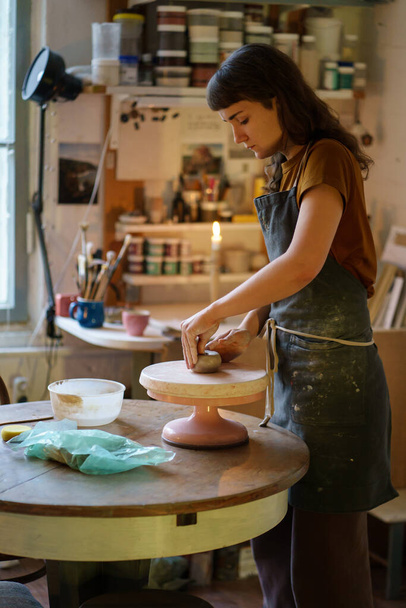 Young female potter maker work with clay on pottery wheel in creative space or professional studio - Photo, image