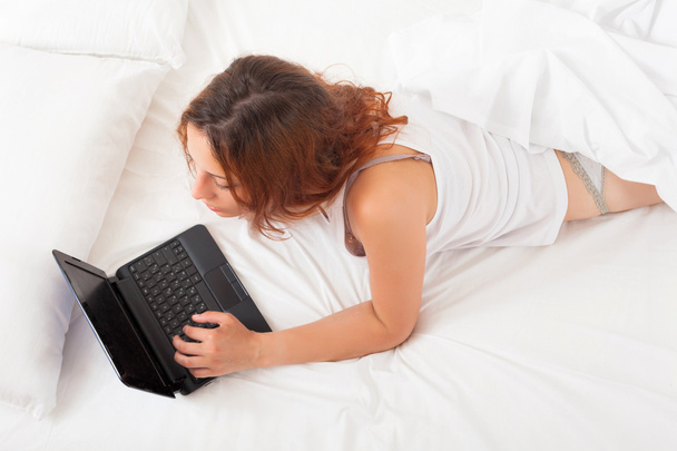 girl with laptop lying on white sheet   - Foto, Imagen