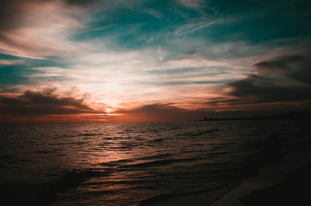 A mesmerizing view of a sea under a cloudy sky at sunset - Photo, image