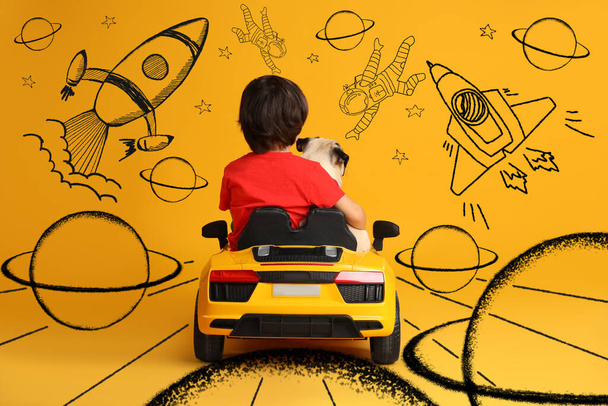 Cute little boy with his dog in toy car and drawing of space on yellow background - Fotoğraf, Görsel