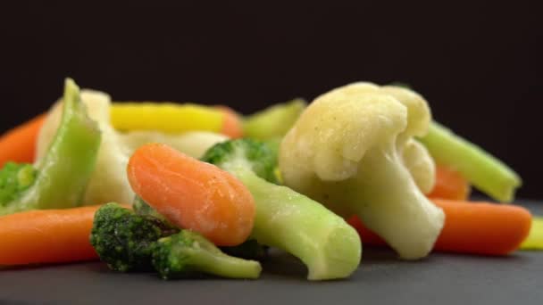 Świeże mrożone warzywa obracające się na czarnym tle, zdrowa żywność lub dieta dla wegetarian i wegan, mrożone kalafiory, brokuły i marchewki dla niemowląt - Materiał filmowy, wideo