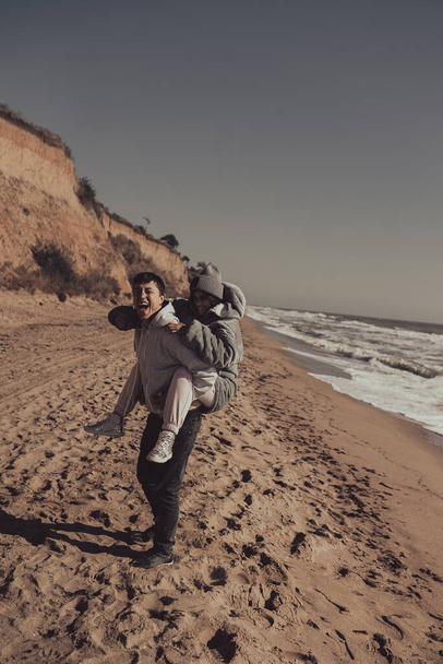 Чоловік носить свою подругу на спині, розважаючись на березі. - Фото, зображення