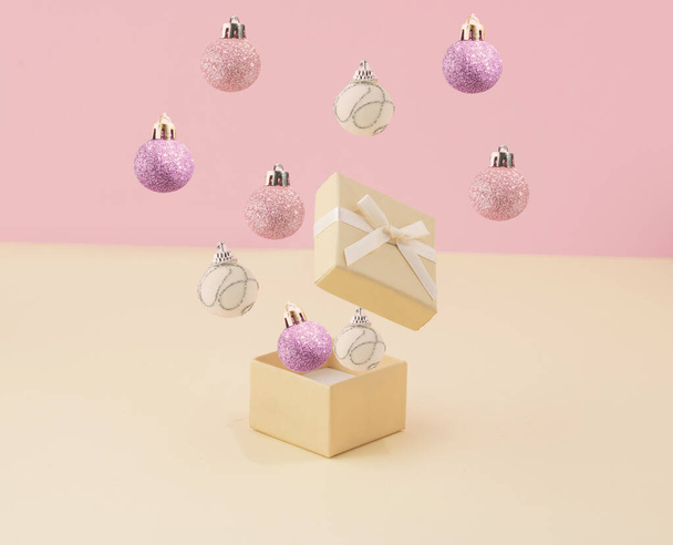 Surprise gift box with christmas bubles against pastel pink and vanilla yellow color background. Creative holiday concept - Фото, изображение