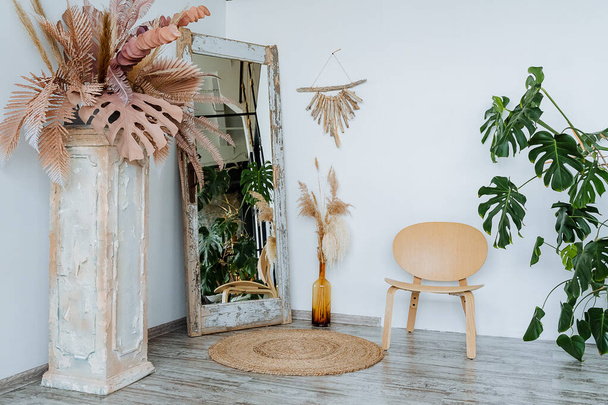 Interior shot. Bright room of the studio.A vase with piles of wheat Interesting wooden table. The main element of the room: a wicker mat. floor mirror and wooden chair. High quality photo - Φωτογραφία, εικόνα