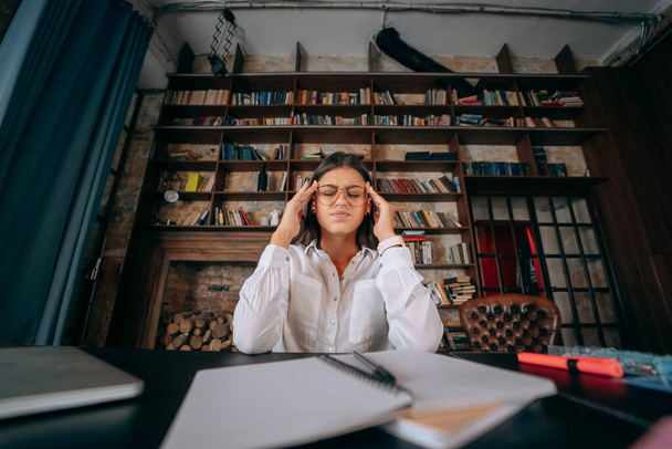 Young woman in office thinking over problem on background of bookshelves - Photo, Image