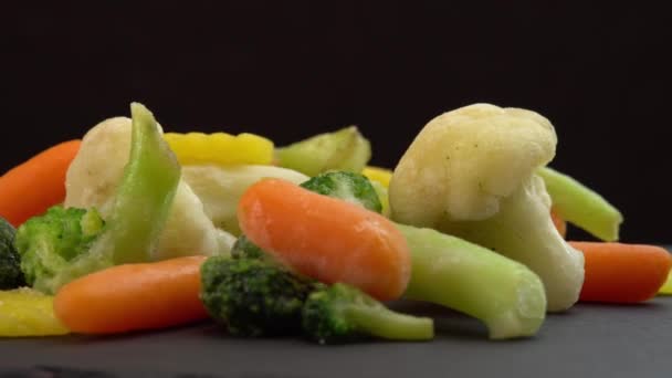 Свіжі заморожені овочі, що обертаються на чорному тлі, здорова їжа або дієтична їжа для вегетаріанців та веганів, заморожена цвітна капуста, броколі та дитяча морква
 - Кадри, відео