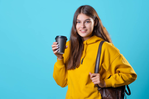Um jovem estudante de capuz amarelo com uma xícara de café de papelão para levar. - Foto, Imagem