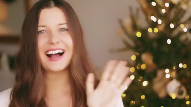 Weihnachts- und Urlaubsgrüße. Glückliche Frau lächelnd und winkende Hand, geschmückte Weihnachtsbaumbeleuchtung im Hintergrund - Filmmaterial, Video