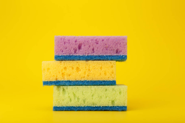 Green, purple and yellow cleaning and dishwashing sponges on yellow background. Close up, dishwashing or house cleaning concept - 写真・画像