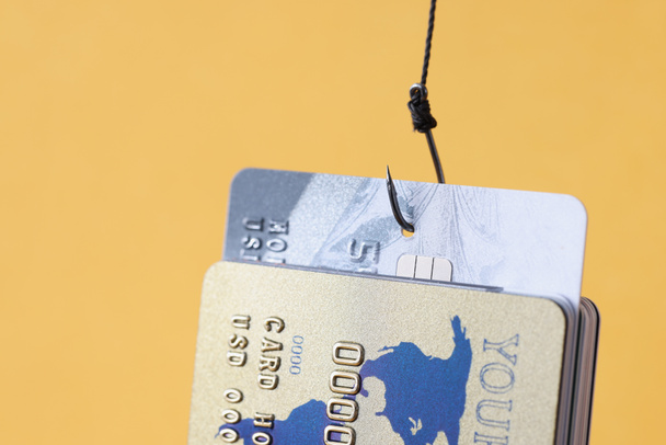 Πολλές τραπεζικές κάρτες κρέμονται στο αγκίστρι αλιείας σε κίτρινο φόντο closeup - Φωτογραφία, εικόνα