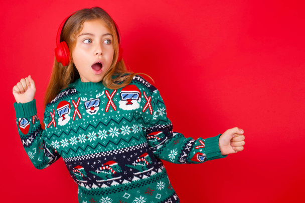 beautiful girl wearing christmas sweater   dancing and listening music with headphones. - Photo, image