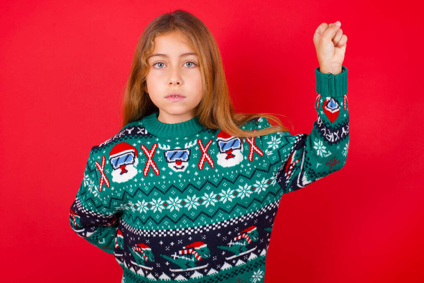 schönes Mädchen im Weihnachtspullover, das sich ernst, stark und rebellisch fühlt, die Faust erhebt, protestiert oder für die Revolution kämpft. - Foto, Bild