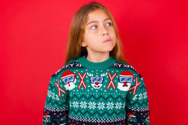 όμορφο κορίτσι φορώντας χριστουγεννιάτικο πουλόβερ φαίνεται επιπόλαια στην άκρη, σχεδιάζει δράσεις μετά το πανεπιστήμιο, φαντάζεται τι να κάνει Σκέφτεται πάνω για το νέο έργο. - Φωτογραφία, εικόνα