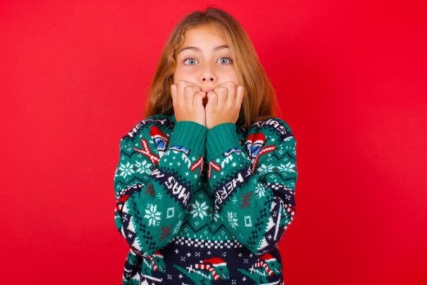 Ansia - bella ragazza che indossa maglione di Natale che copre la bocca con le mani spaventate da qualcosa o qualcuno che morde le unghie. - Foto, immagini
