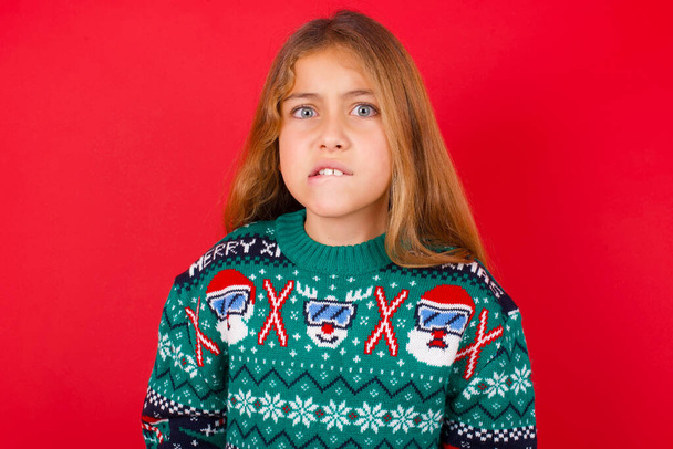 красива дівчина в різдвяному светрі нервує і наляканий кусаючи губи дивиться в камеру з нетерплячим виразом, стомлює. - Фото, зображення
