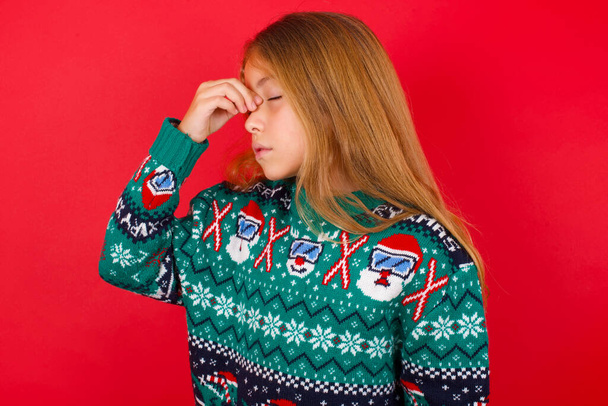 Дуже засмучена, красива дівчина в різдвяному светрі торкається носа між закритими очима, хоче плакати, мати стресові відносини або мати проблеми з роботою - Фото, зображення