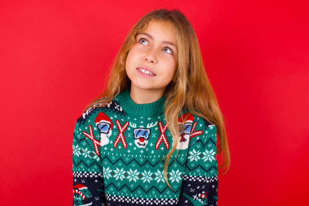 Portret tajemniczej pięknej dziewczyny noszącej świąteczny sweter spoglądającej w górę z enigmatycznym uśmiechem. Koncepcja reklamy. - Zdjęcie, obraz