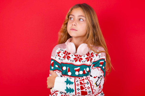 Příjemná krásná dívka na sobě vánoční svetr udržuje ruce přes hrudník vypadá šťastně stranou - Fotografie, Obrázek
