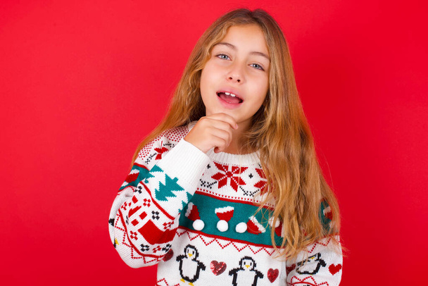 schönes Mädchen im Weihnachtspullover lacht glücklich hält die Hand am Kinn drückt positive Emotionen aus Lächeln hat unbeschwerten Ausdruck - Foto, Bild