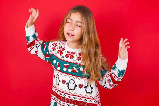 Photo of upbeat  beautiful girl wearing christmas sweater   has fun and dances carefree wear being in perfect mood makes movements. Spends free time on disco party - Foto, Imagem