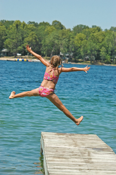 mladá dívka skočí z doku se zbraněmi a roztaženýma nohama - Fotografie, Obrázek