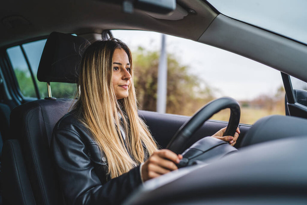 Jeune adulte une femme caucasienne conduisant voiture en attente tout en tenant volant regardant sur la route vue de côté femme conducteur copier l'espace personnes réelles embouteillage - Photo, image
