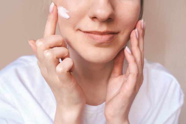 Beautiful smiling girl applying cream on face. Body care concept - Фото, зображення