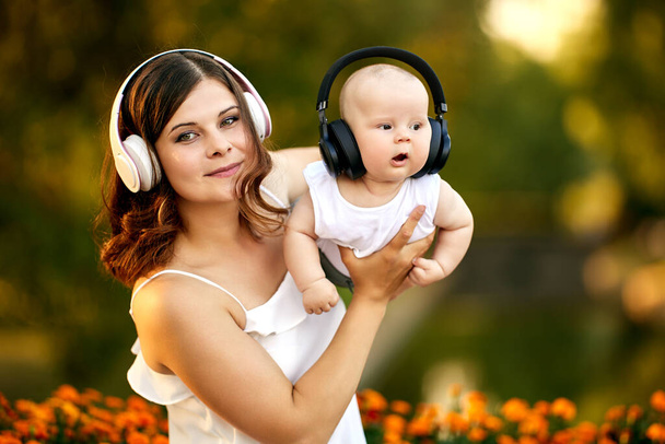 Young mother on maternity leave takes care of baby, mom and son listen to music through wireless headphones. - Foto, imagen