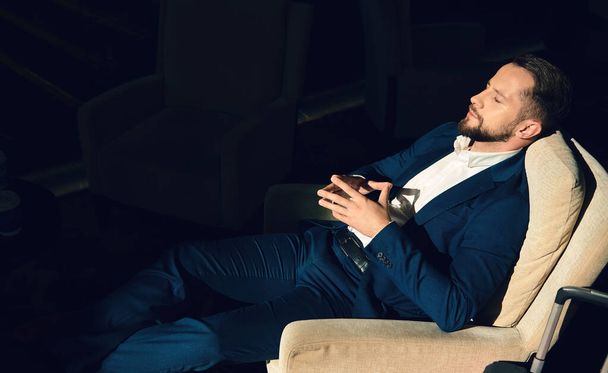 Successful businessman, entrepreneur, traveler on business trip, leaning on the back of an armchair, resting with closed eyes in the hotel lounge, exhausted after negotiations and business meetings - Photo, Image