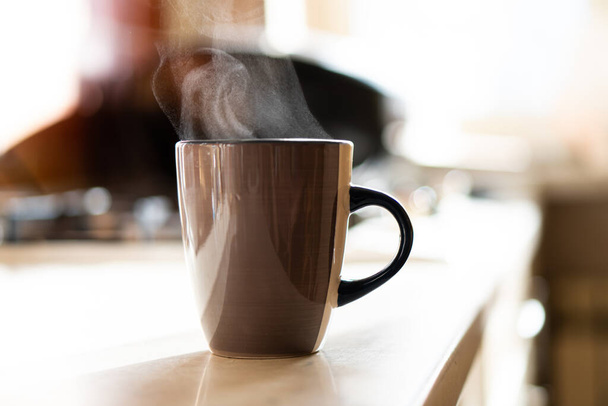 Tasse à café marron sur table de cuisine avec lumière naturelle et vapeur - Photo, image