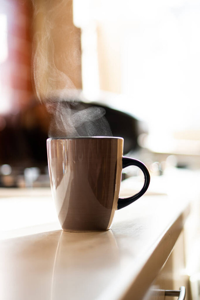 Brown coffee cup on kitchen table with real natural daylight and steam - Photo, Image