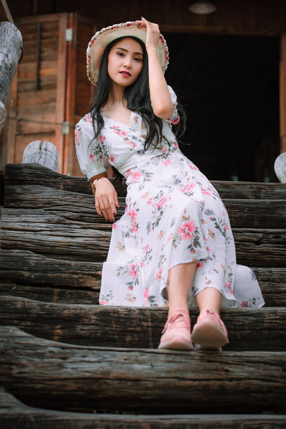 Beautiful young asian women in retro flowers pink dresses styles and hat vintage sitting on wooden stair front view old house background and looking camera, natural light portrait profile in vacation and retro style ideas  - Фото, изображение
