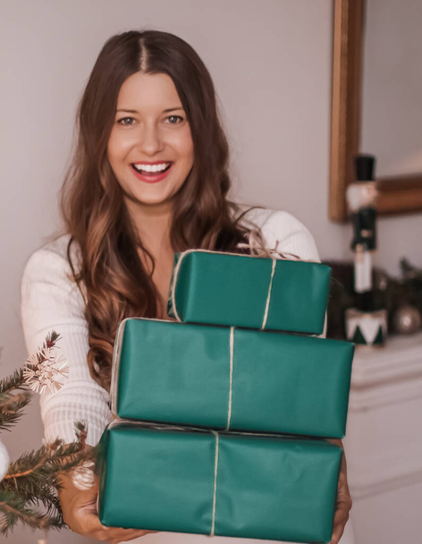 Święta Bożego Narodzenia i zrównoważone prezenty koncepcja. Szczęśliwa uśmiechnięta kobieta trzyma pakowane prezenty z ekologicznym zielonym papierem do pakowania - Zdjęcie, obraz