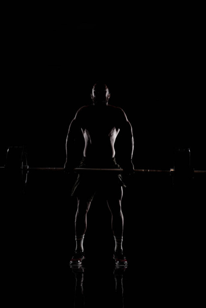 Athlete lifting barbell. Silhouette of a muscular man. - Φωτογραφία, εικόνα