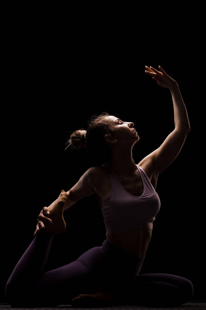 Fit girl practicing yoga in a studio. Half silhouette side lit fitness model - 写真・画像