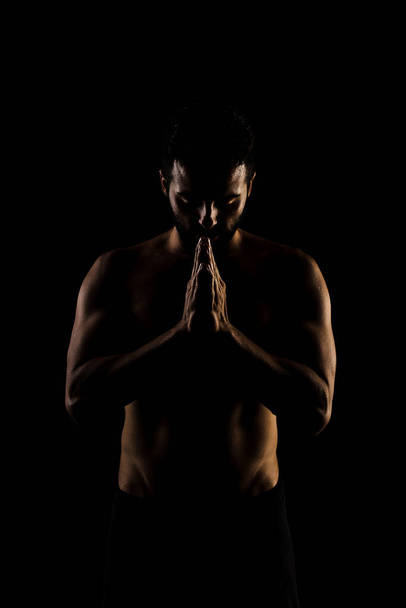 Side lit muscular Caucasian man silhouette. Athlete praying against black background.  - Fotografie, Obrázek